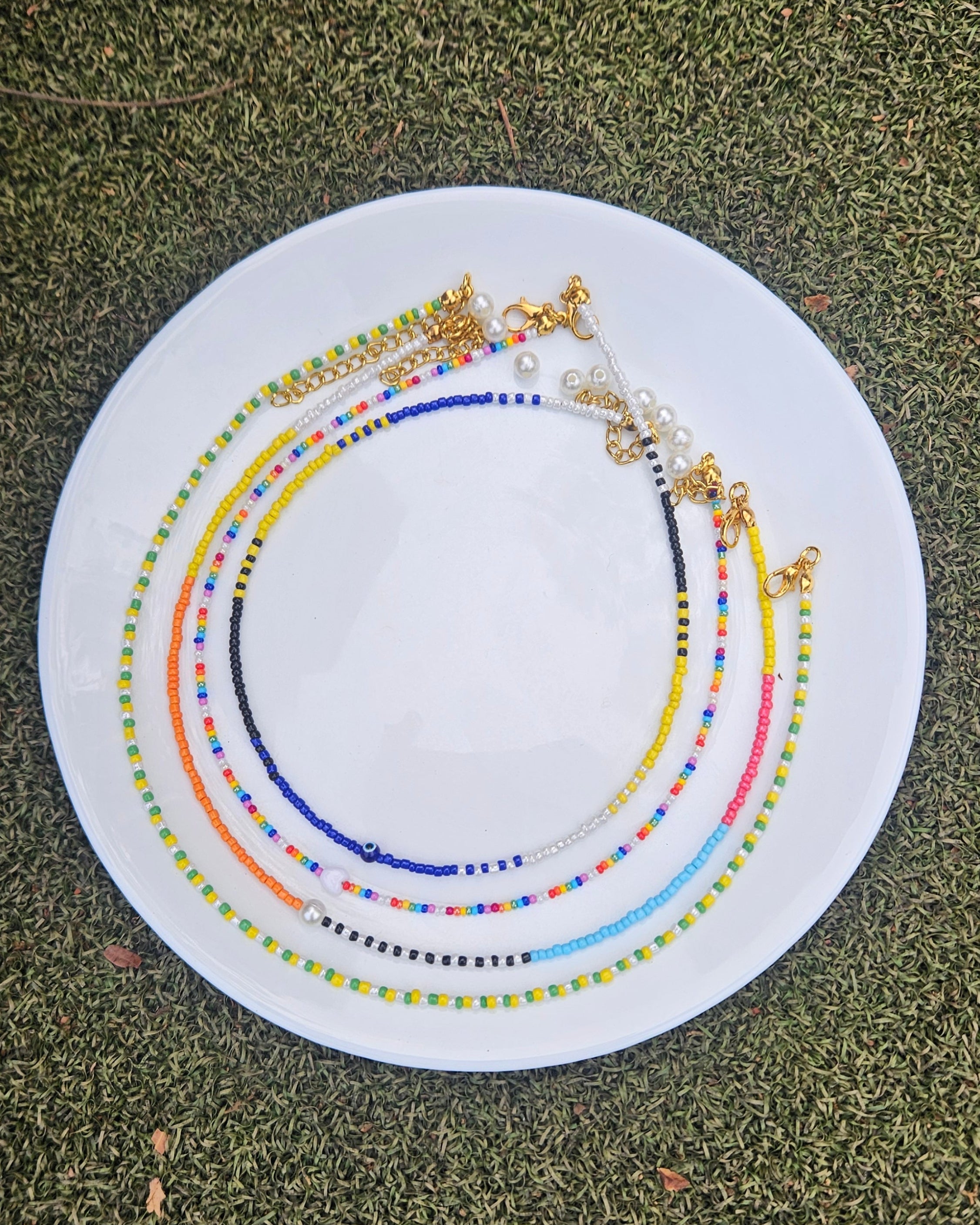 Set of colorful beaded necklaces on a white plate against a green grass background