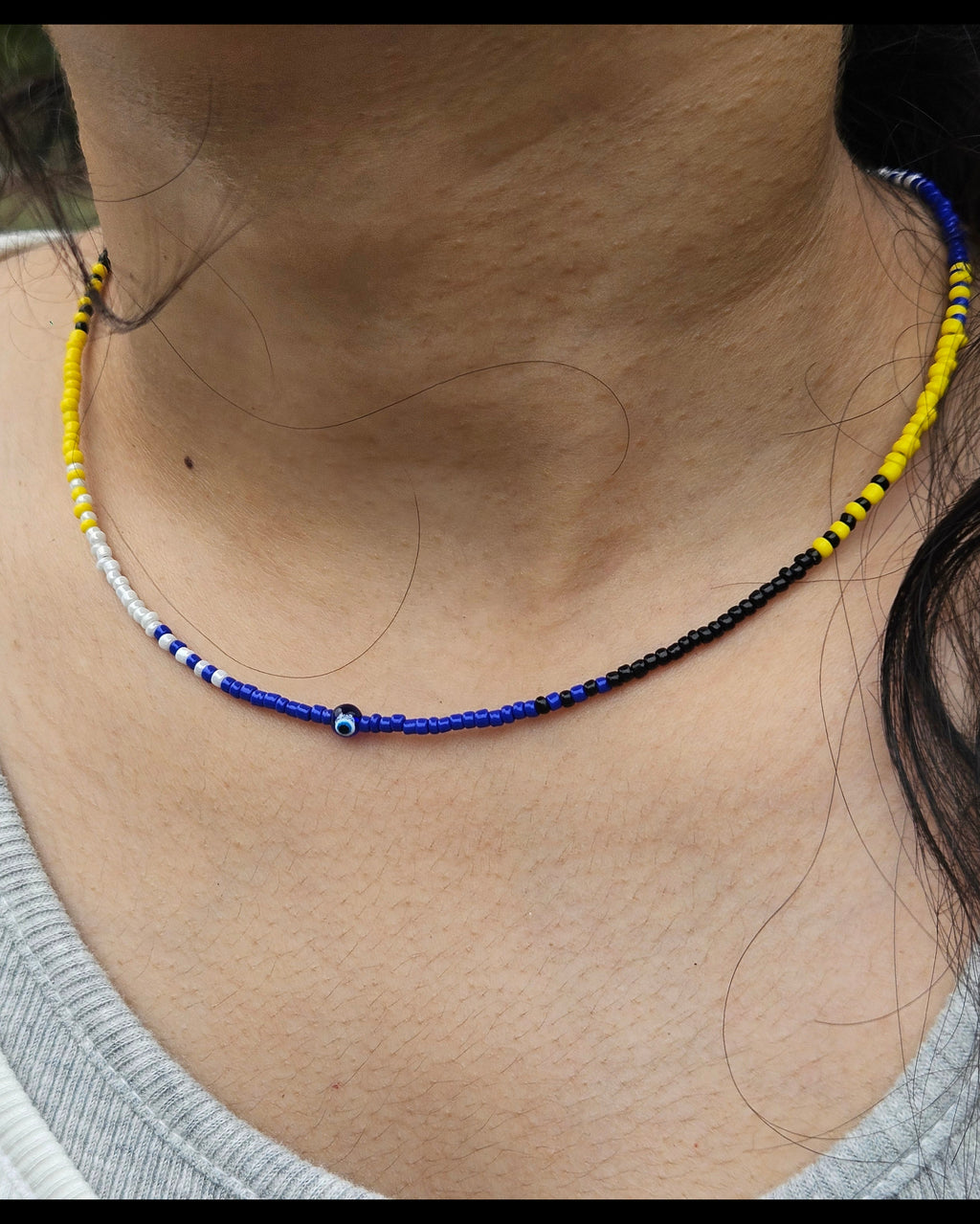 Necklace with blue and yellow beads on a person wearing a white shirt.
