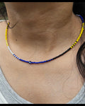 Necklace with blue and yellow beads on a person wearing a white shirt.
