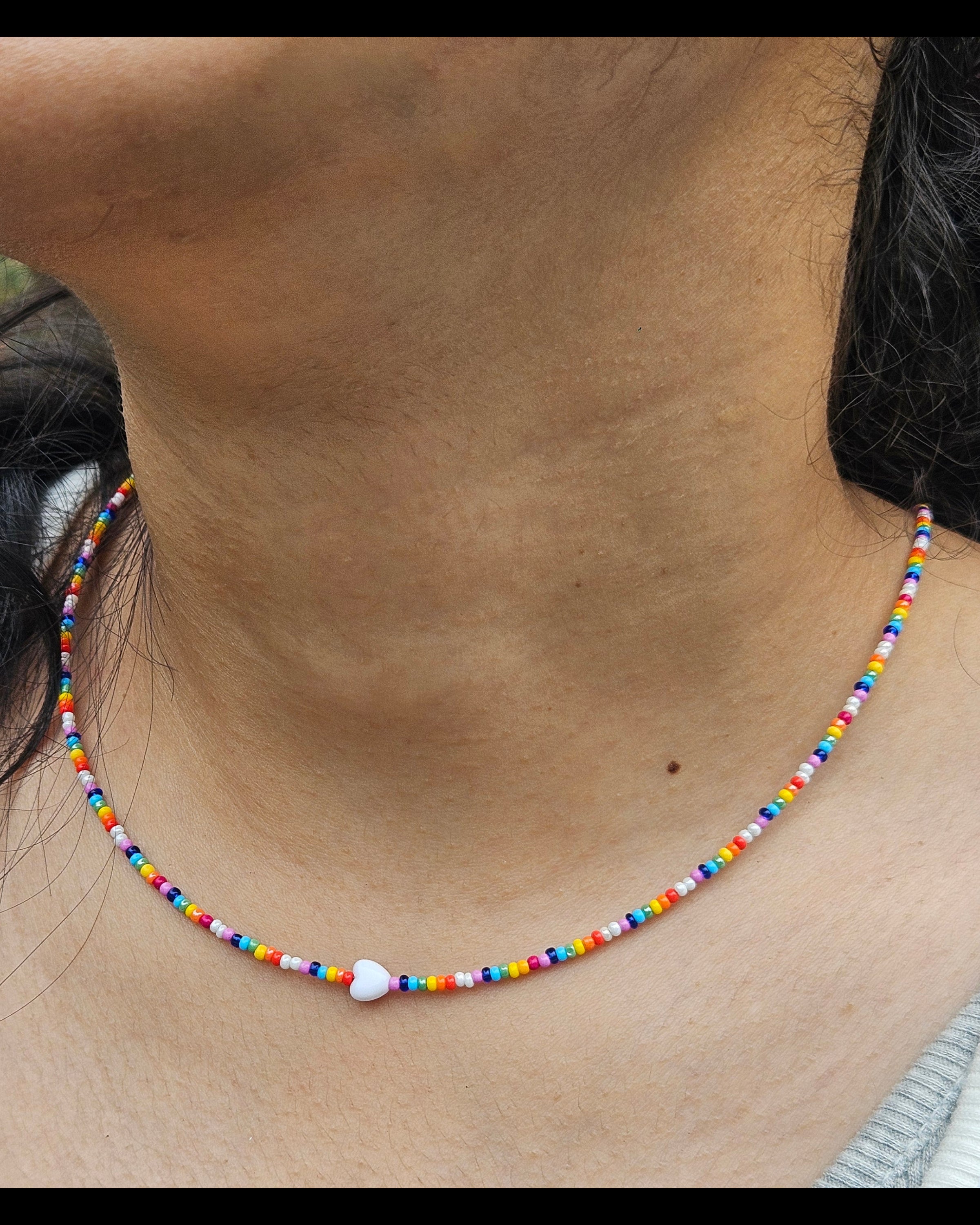 Close-up of a colorful beaded necklace on a person's neck with a blurred outdoor background.