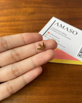 Gold crown earring held between fingers on a wooden surface with AMASO card in the background