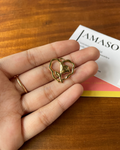 Gold heart-shaped pendant held in a hand on a wooden surface with 'AMASO' book in the background.