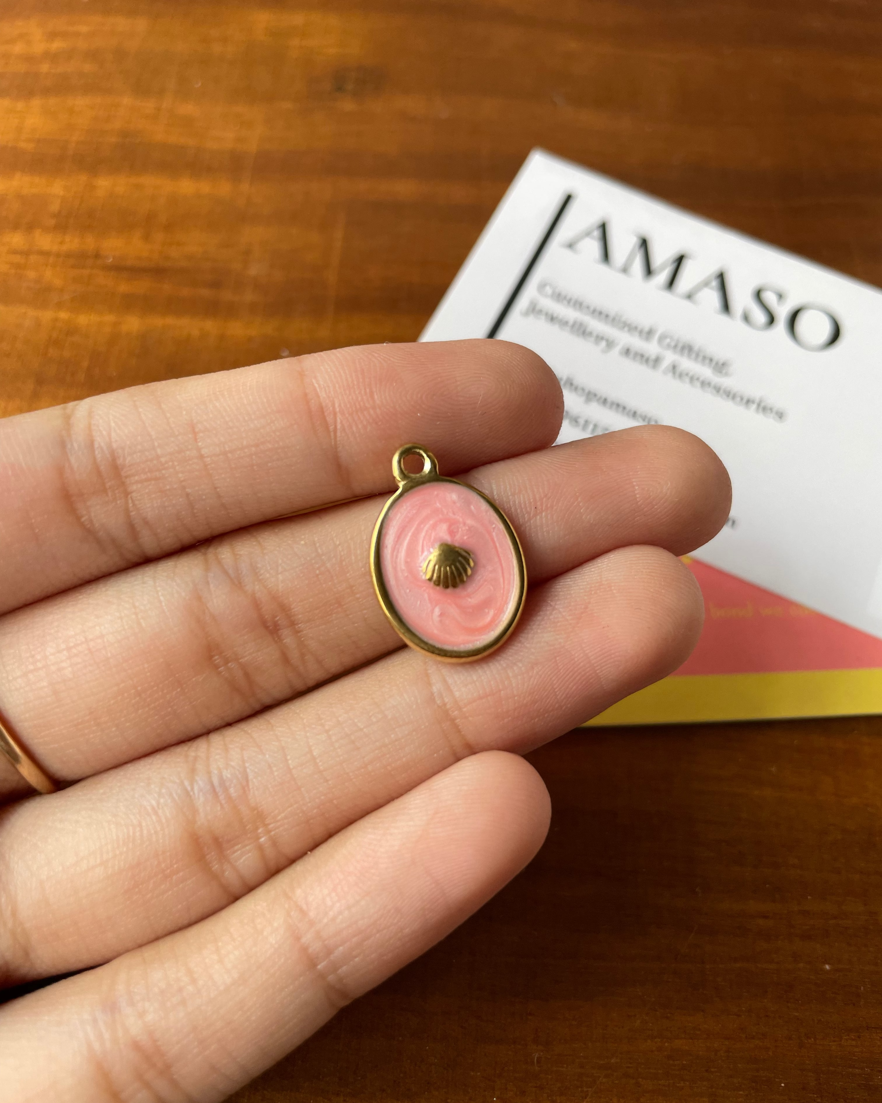 Pink shell pendant on a hand with AMASO branding in the background