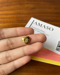 Gold heart-shaped pendant held between fingers with a 'Jamaso' card in the background.