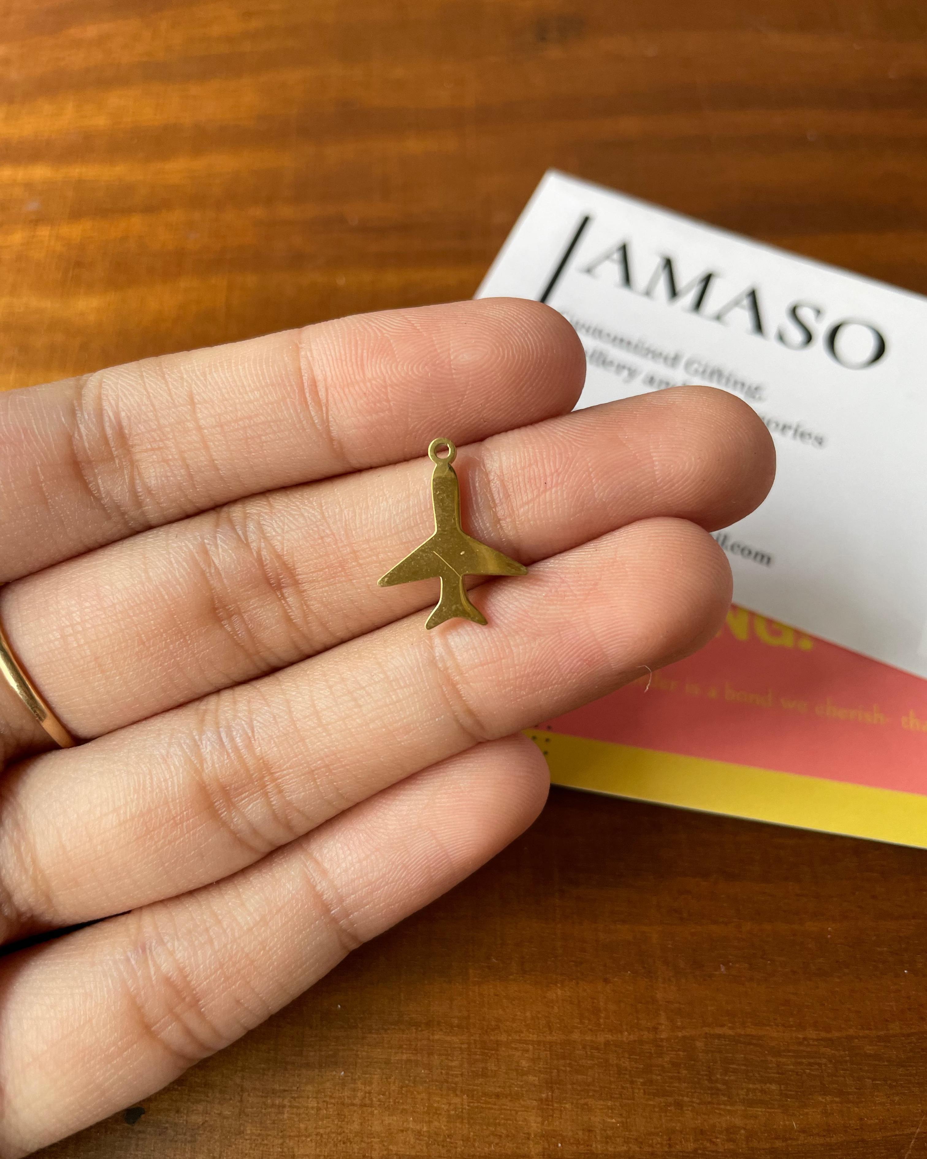 Gold airplane charm held between fingers with a book titled 'JAMASO' in the background.