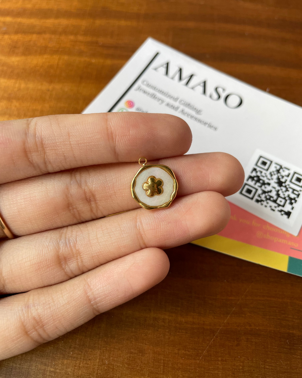 Gold and white pendant held between fingers with AMASO card in background