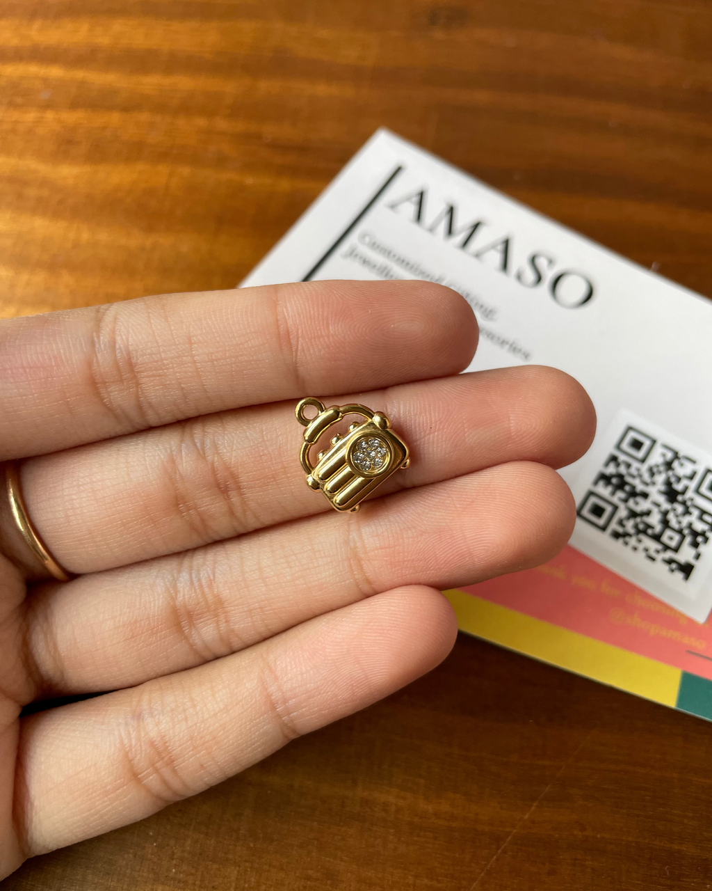 Gold charm held between fingers with a colorful card in the background