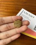 Gold pendant held in a hand with a 'AMASO' card in the background