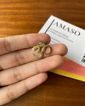 Gold Om pendant held in a hand with AMASO branding in the background