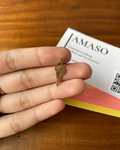 Hand holding a small gold leaf-shaped pendant with a JAMASO product card in the background.