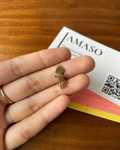 Gold squid-shaped earring held between fingers with a 'AMASO' card in the background.