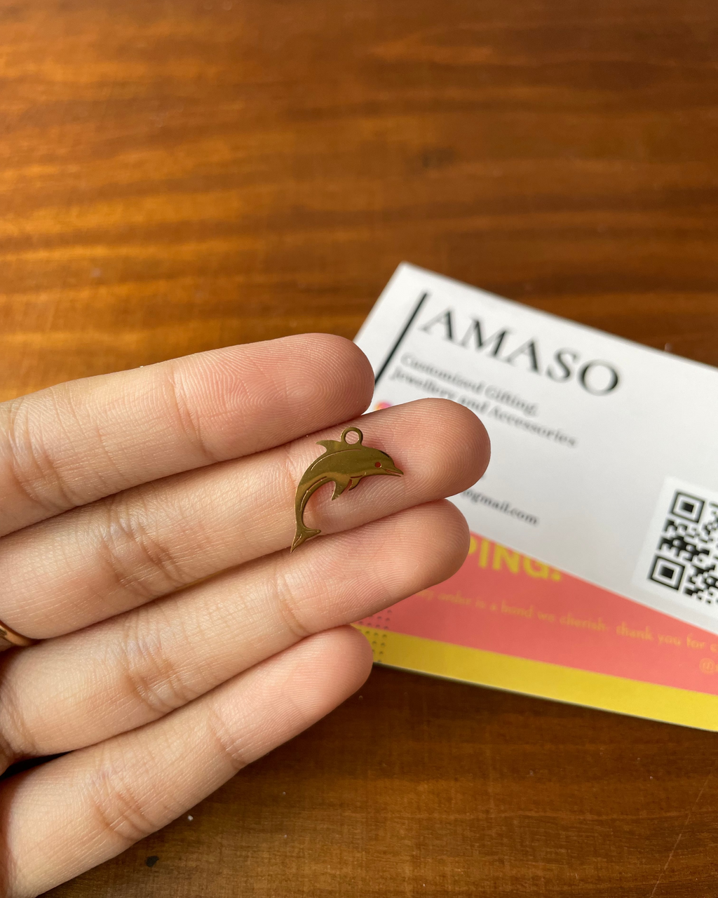 Hand holding a gold dolphin charm with a business card in the background