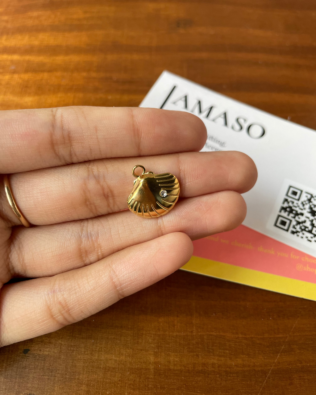 Gold shell pendant held between fingers with a branded card in the background