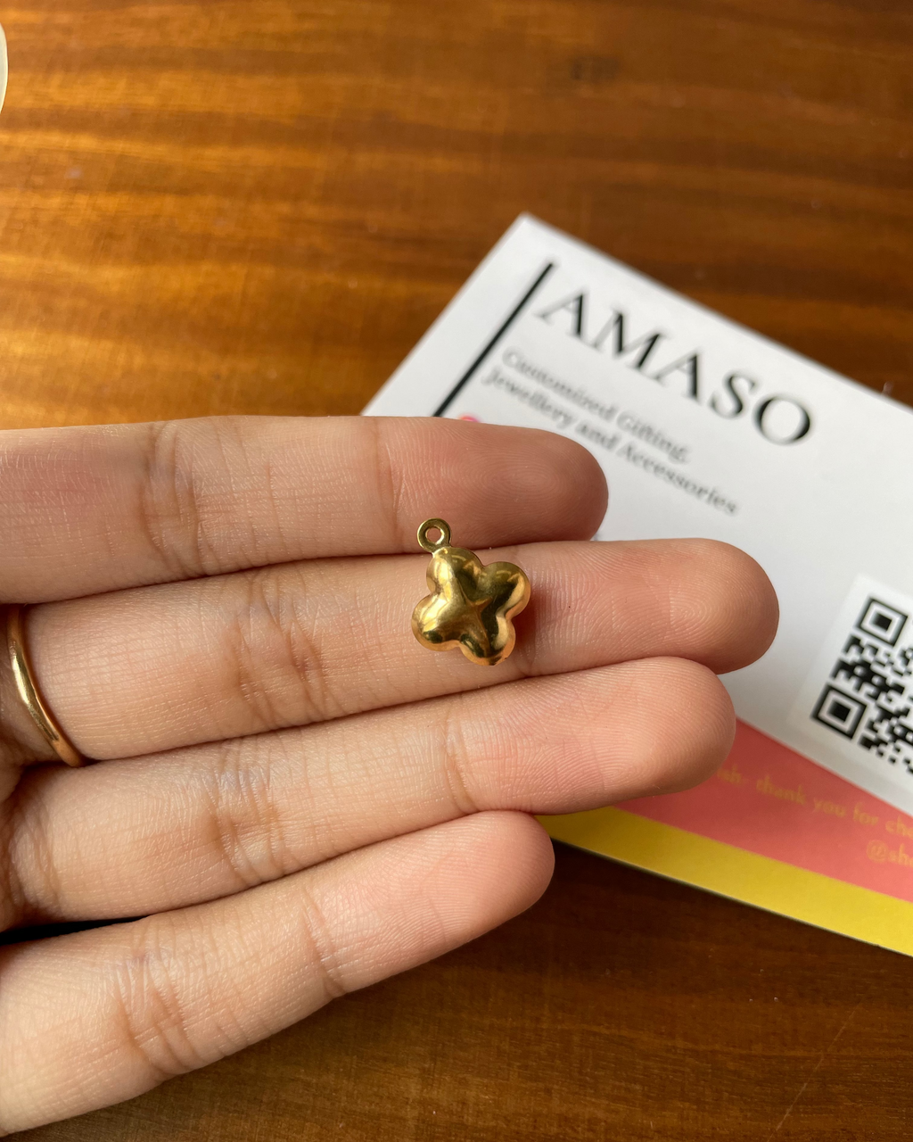 Gold four-leaf clover charm held between fingers with AMASO card in background