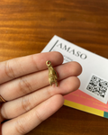 Gold hand-shaped charm held in a hand with a 'JAMASO' card in the background.