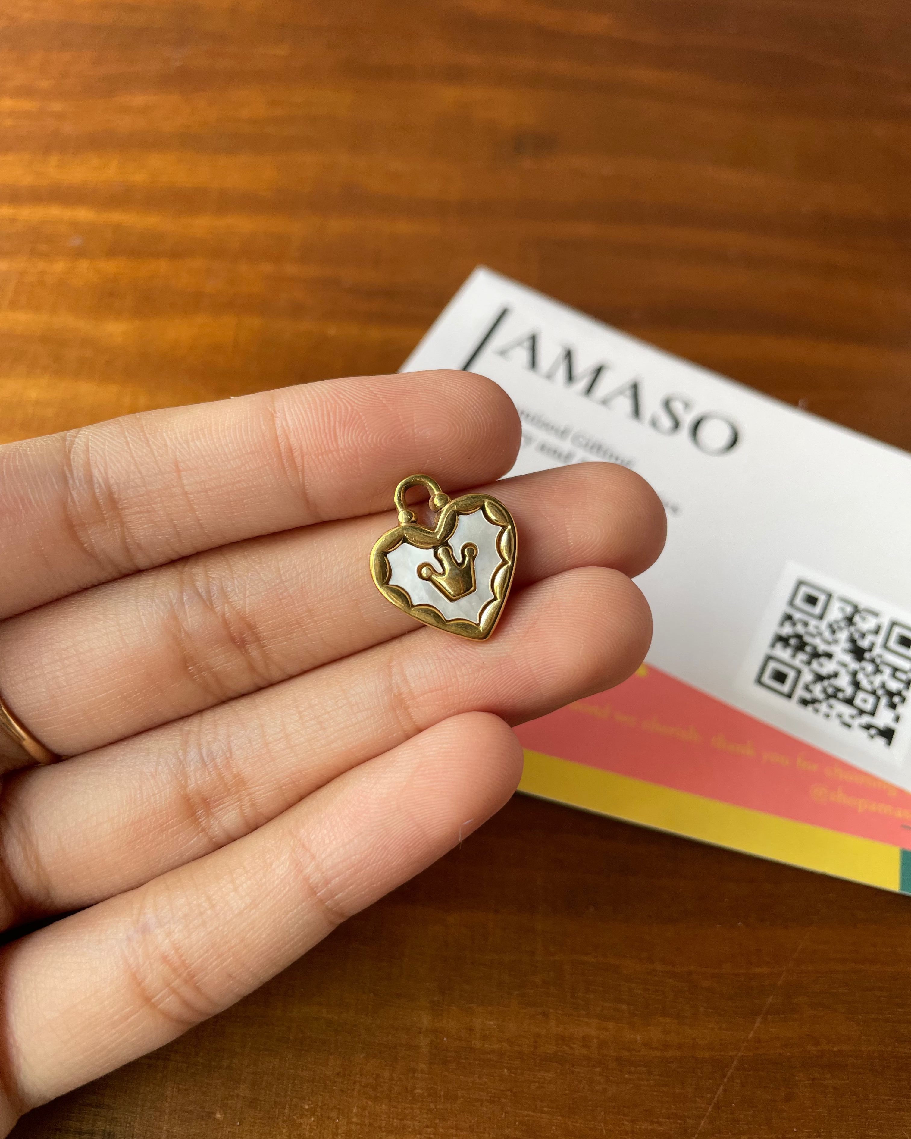 Heart-shaped pendant held in a hand with a JAMASO product in the background