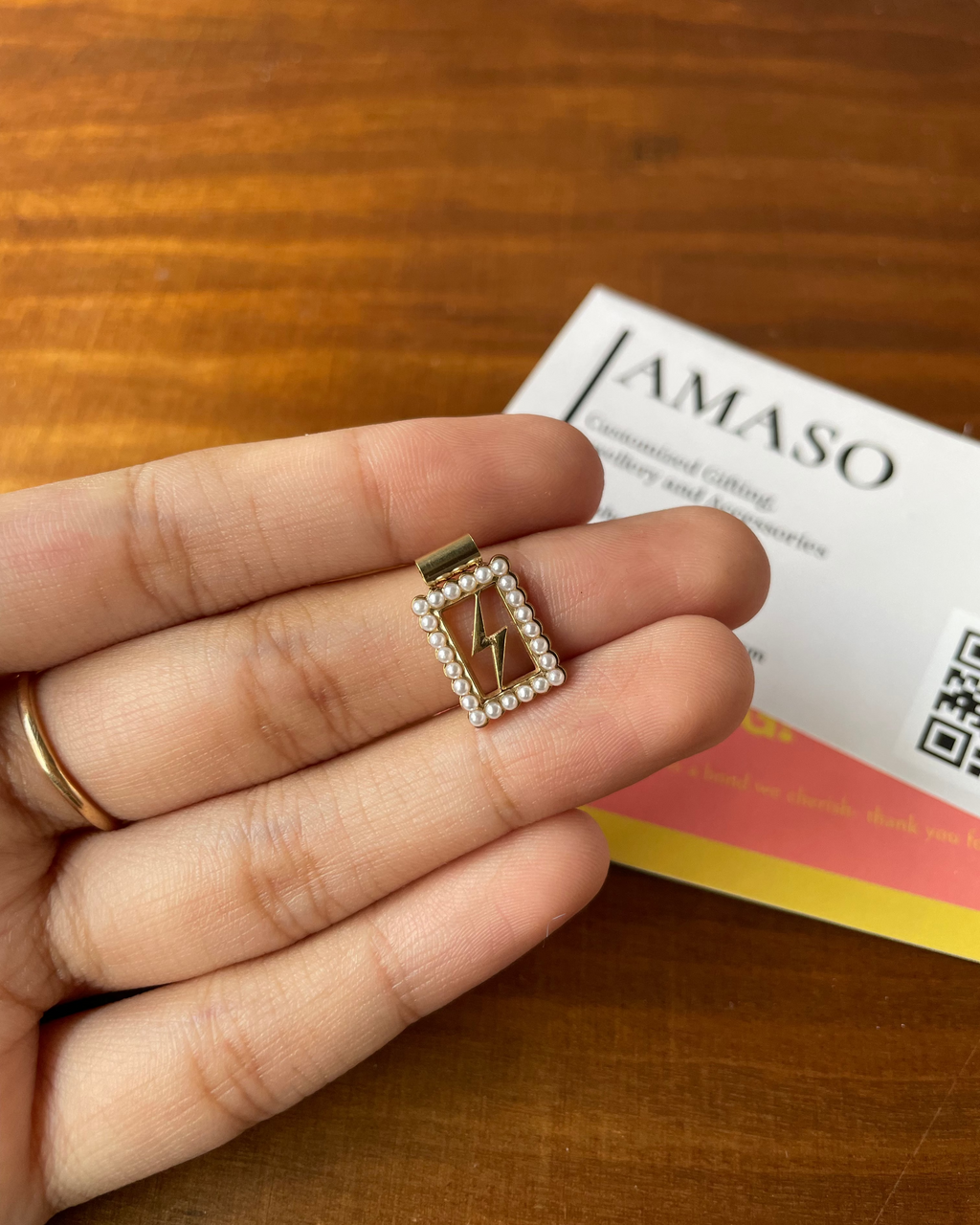 Small decorative item held between fingers with AMASO card in the background