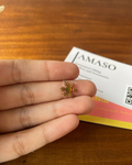 Small gold snowflake charm held between fingers with a 'AMASO' card in the background on a wooden surface.
