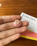 Pink and gold decorative item held between fingers with a blurred 'JAMASO' card in the background.