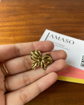 Gold bow-shaped earring held between fingers on a wooden surface with a card in the background.