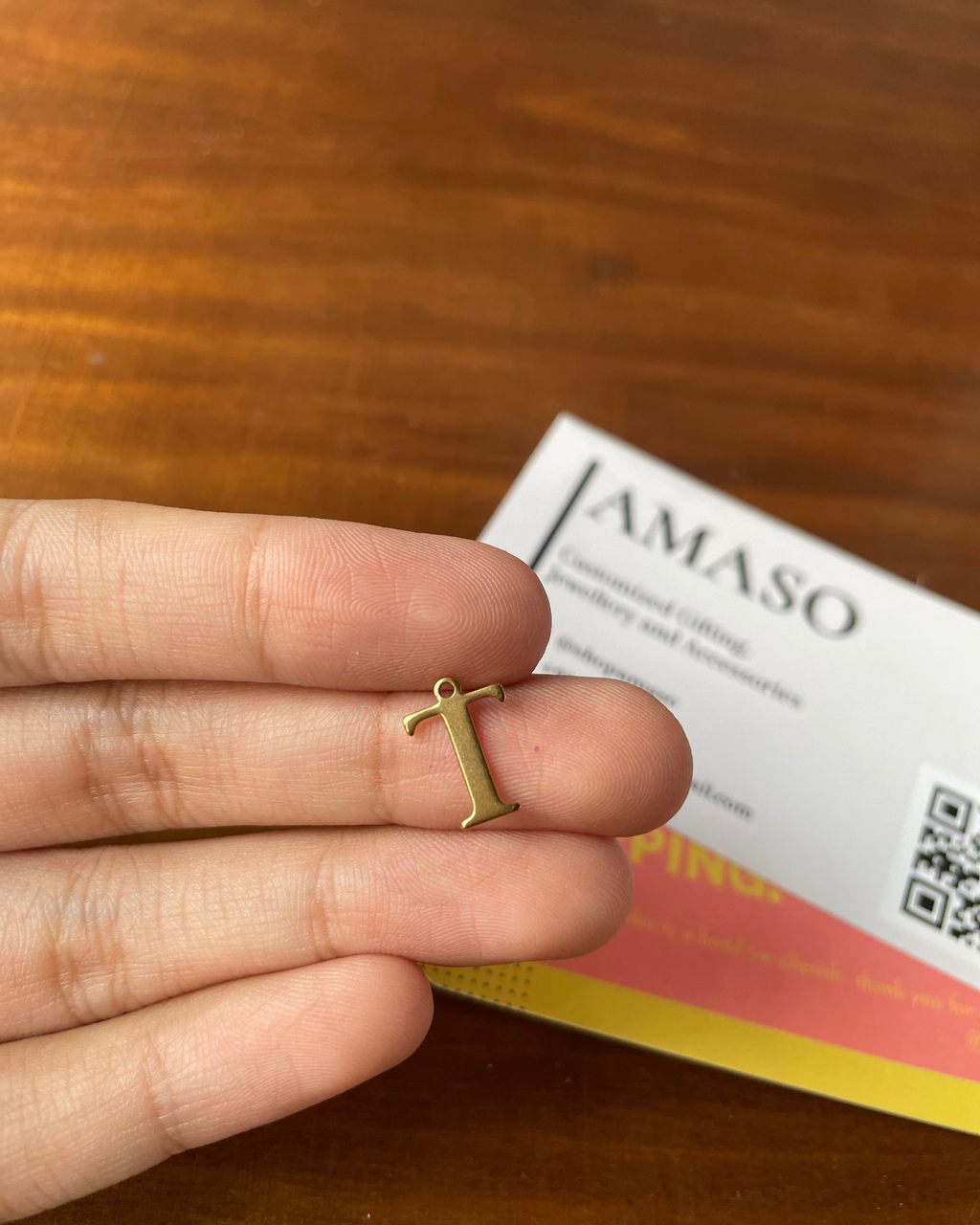 Gold letter 'T' charm held between fingers with AMASO card in the background