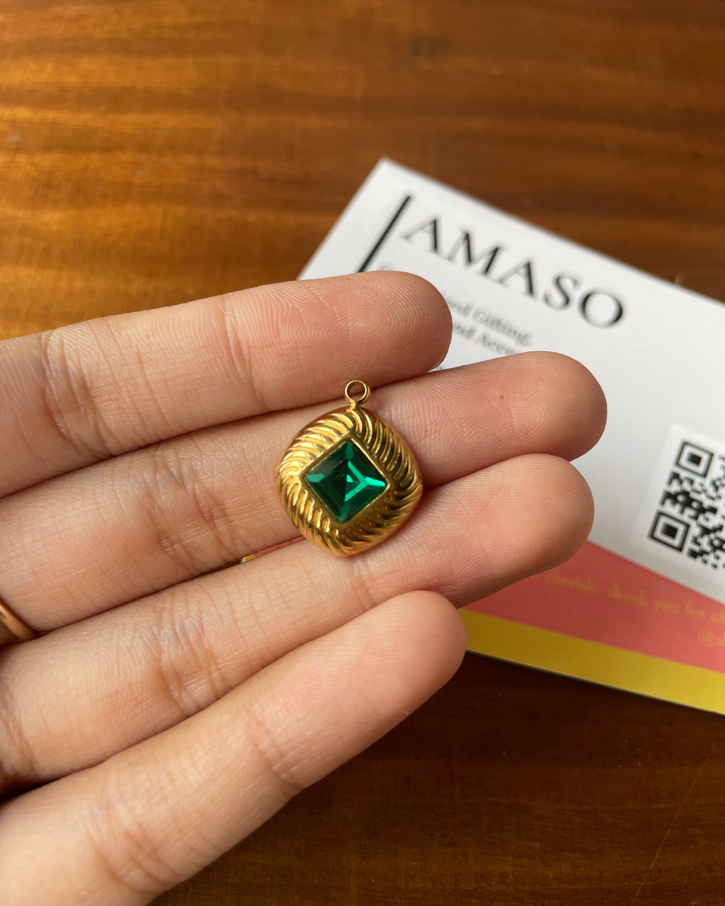 Gold pendant with a green gemstone held in a hand, with a business card in the background.