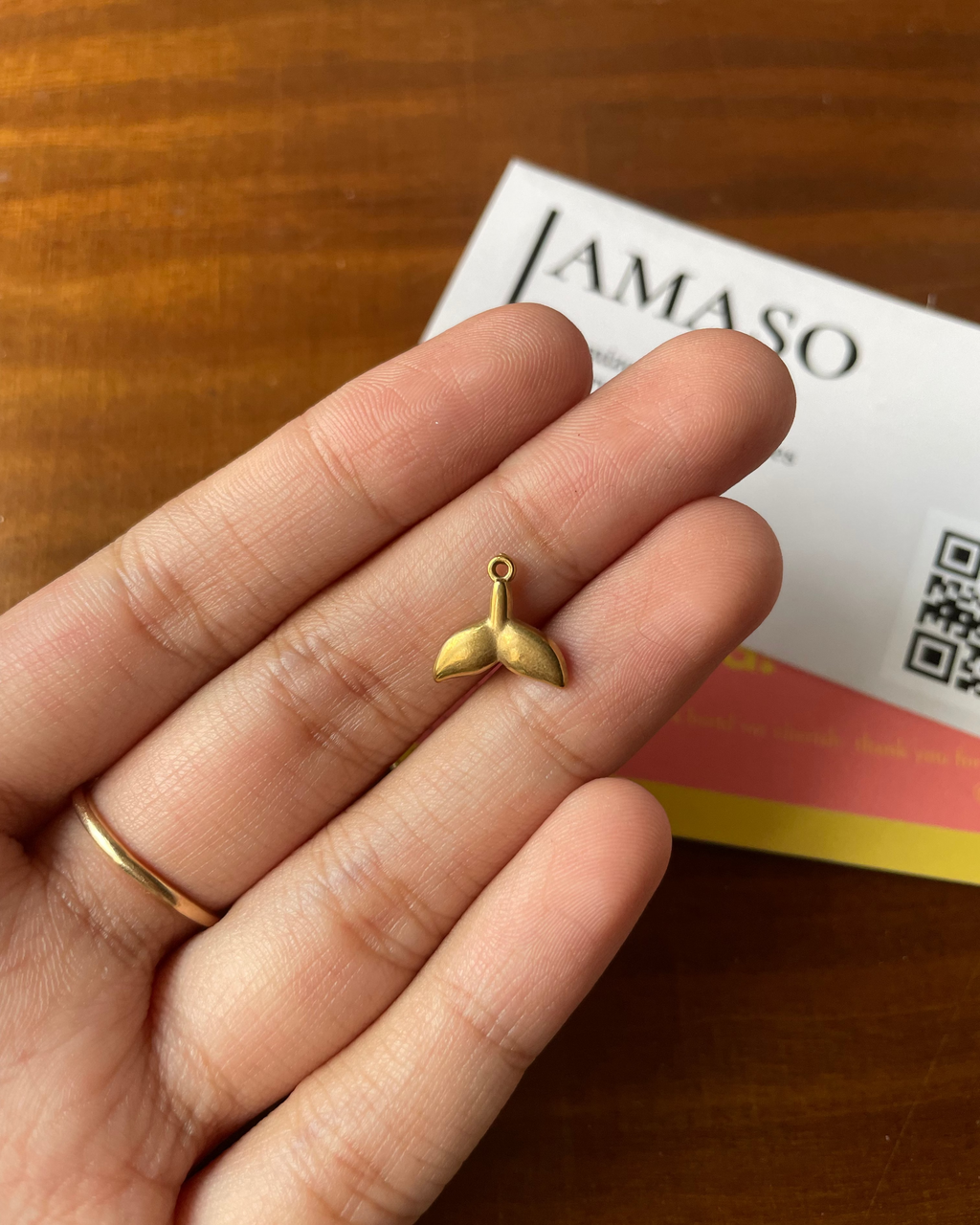 Gold whale tail charm held between fingers with a brand card in the background