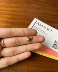 Gold fish-shaped earring on a finger with AMASO jewelry card in the background