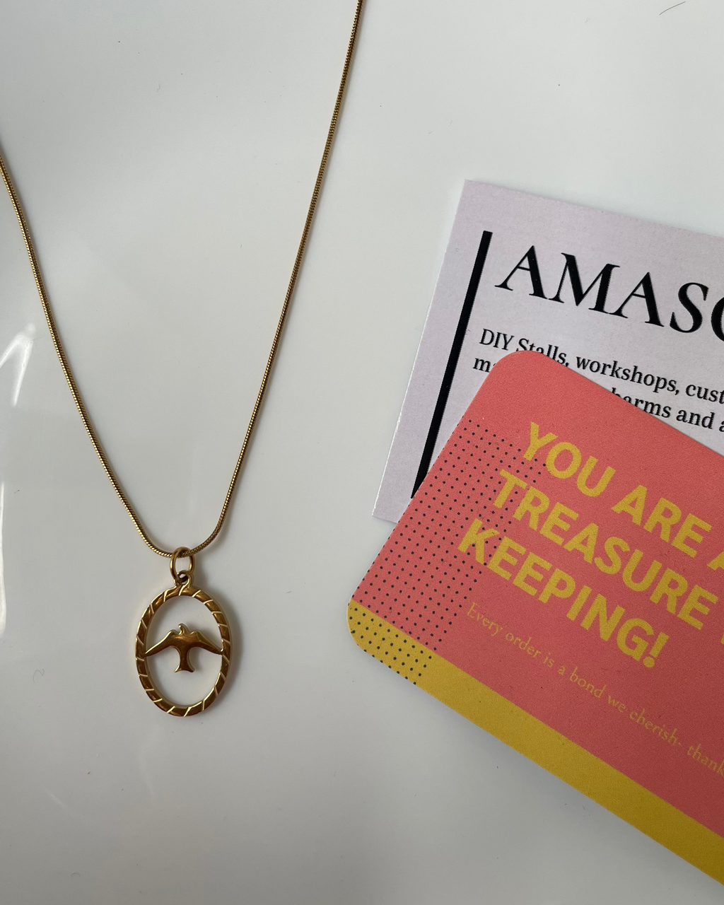 Gold necklace on a white surface with a card featuring 'AMASO' and a motivational message.