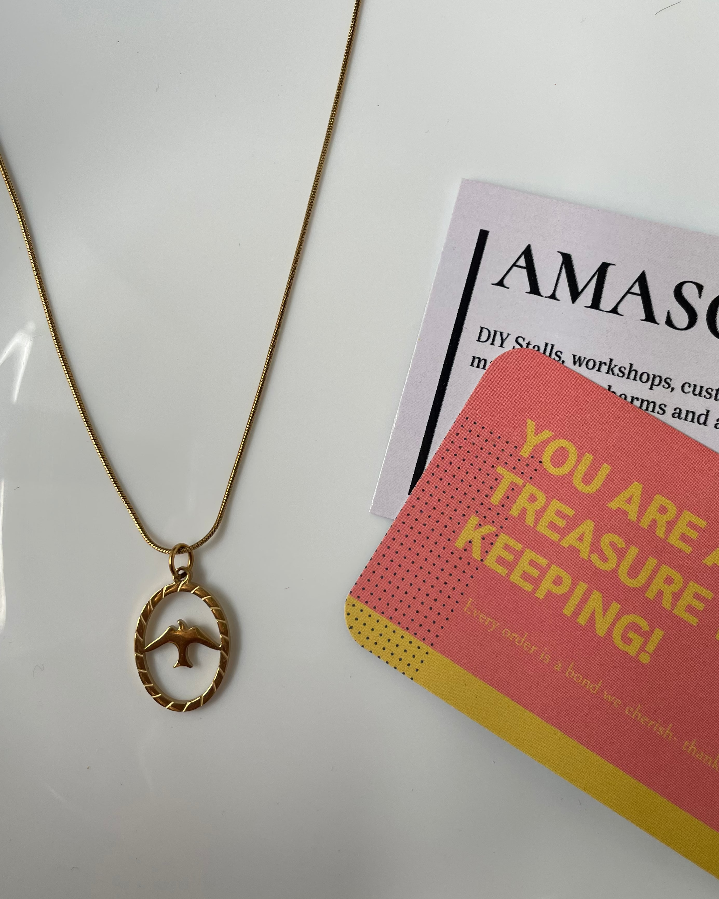 Gold necklace on a white surface with a card featuring 'AMASO' and a motivational message.