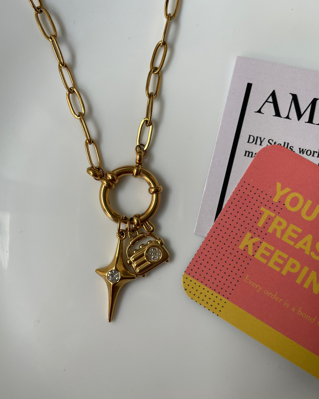 Gold necklace with a star and heart pendant on a white surface with a magazine in the background.