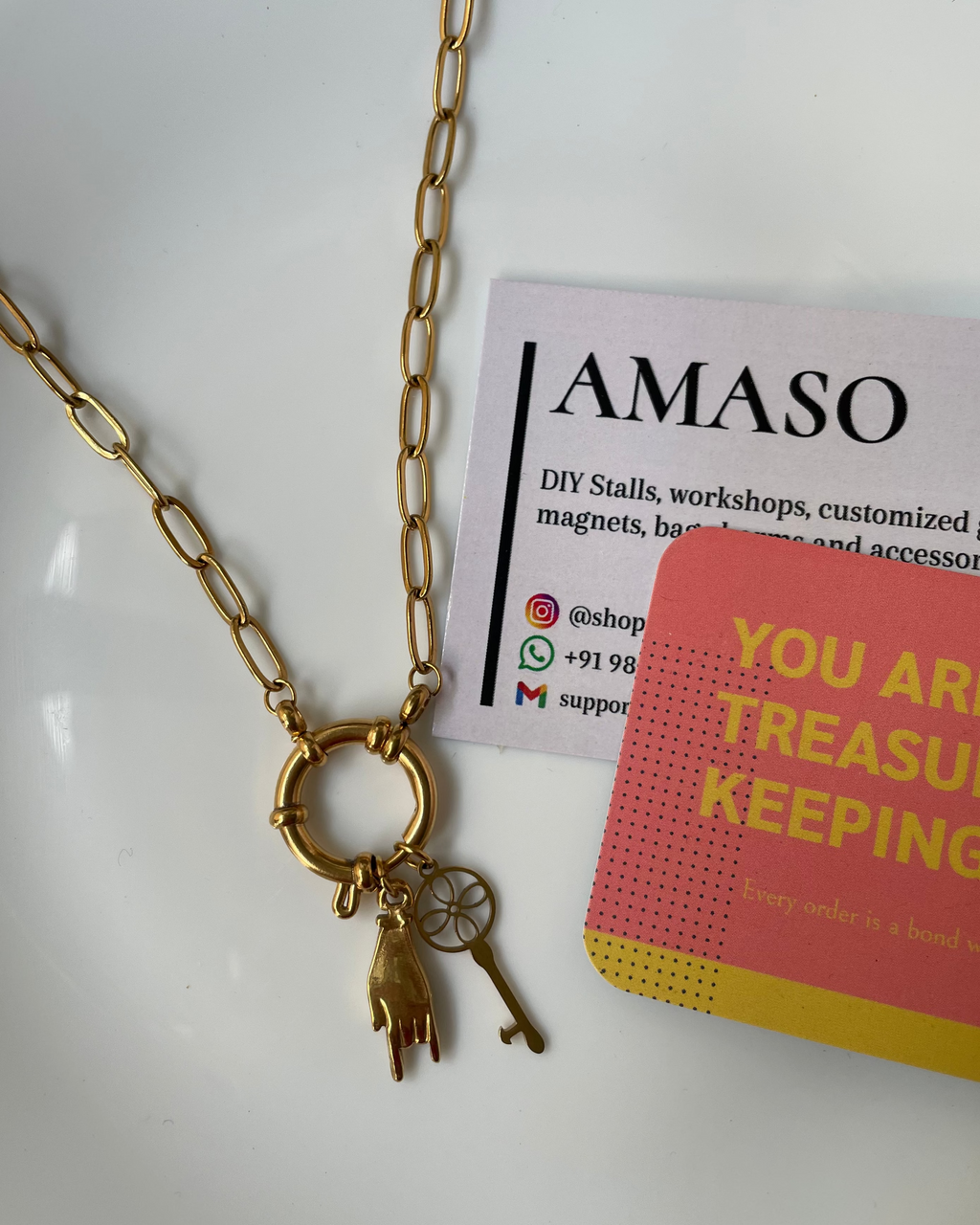 Gold necklace with a key pendant on a white surface with AMASO branding.