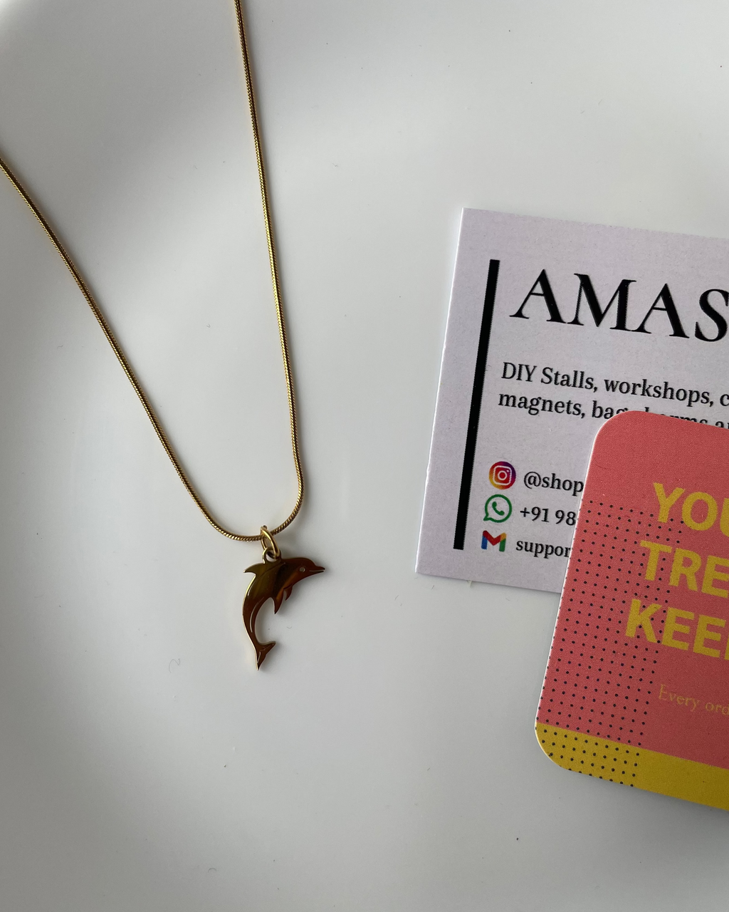 Gold necklace on a white plate with a business card and pink card in the background