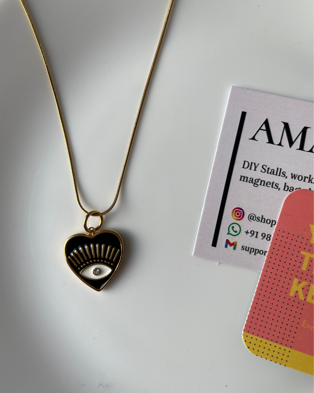 Heart-shaped pendant necklace on a white surface with a business card and phone case.