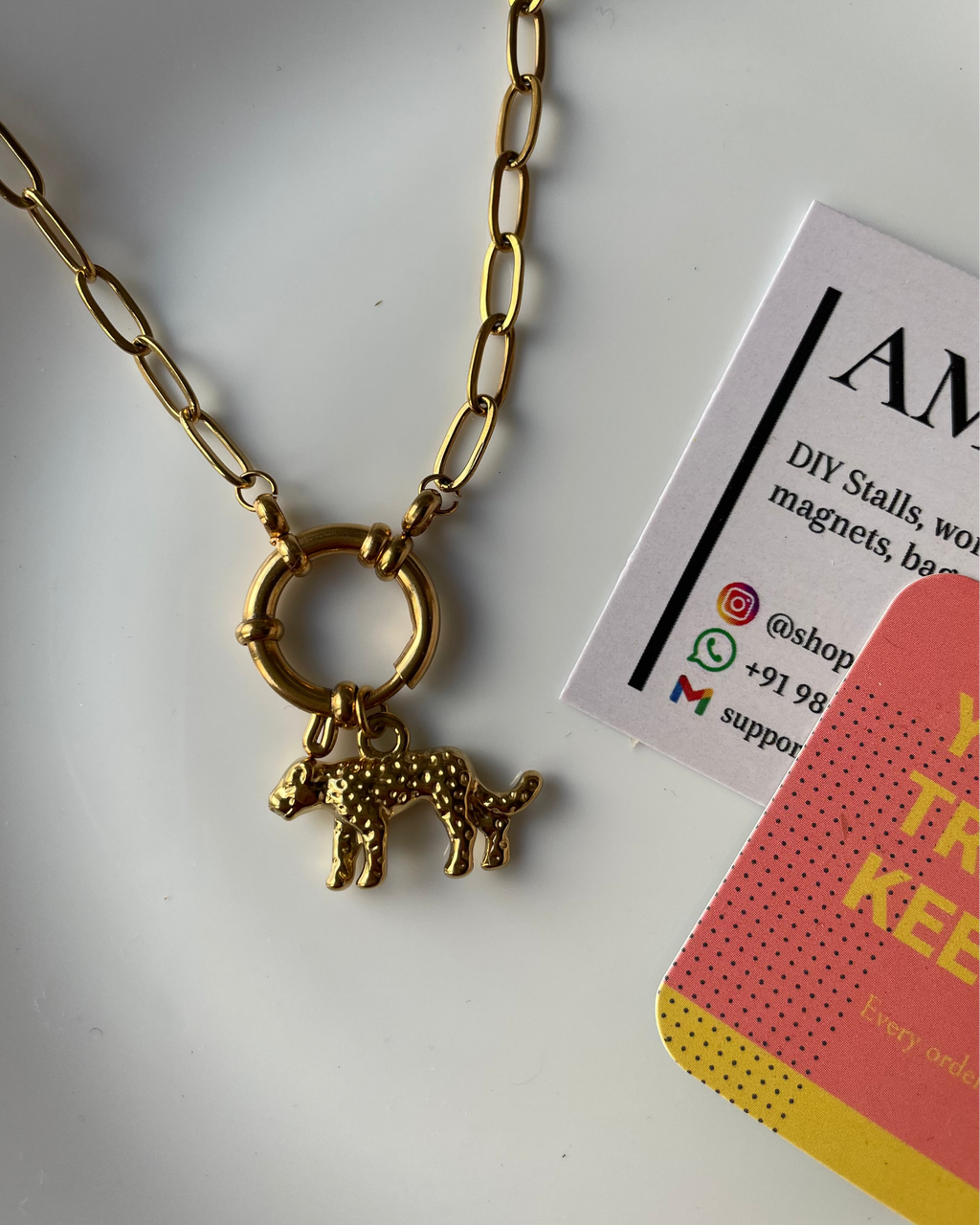 Gold necklace with a bear pendant on a white surface with a business card.