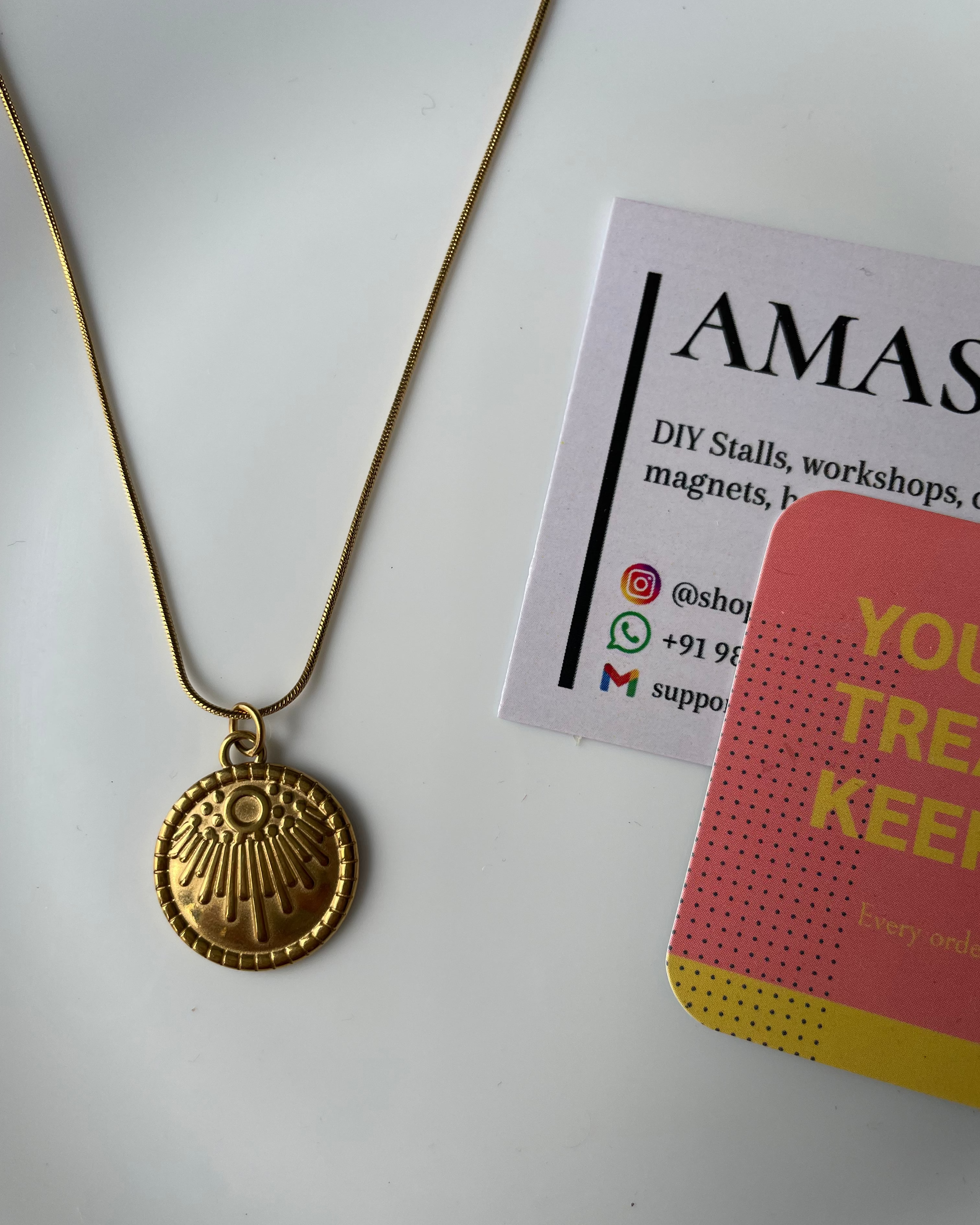 Gold necklace with a pendant on a white surface next to promotional materials.