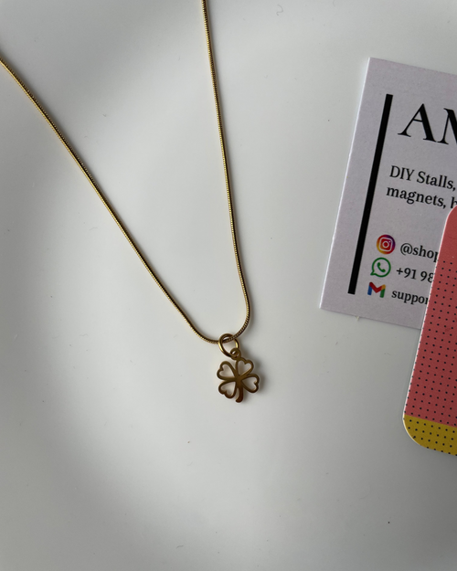 Gold necklace with a clover pendant on a white surface with a business card.
