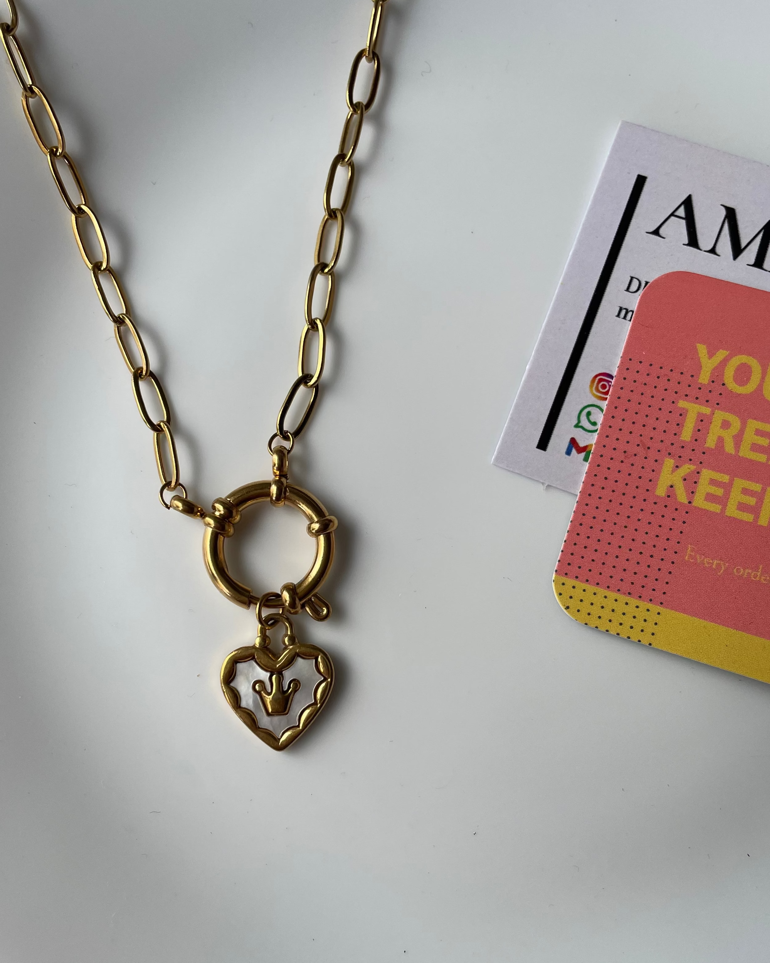 Gold chain necklace with a heart pendant on a white plate with a magazine underneath.