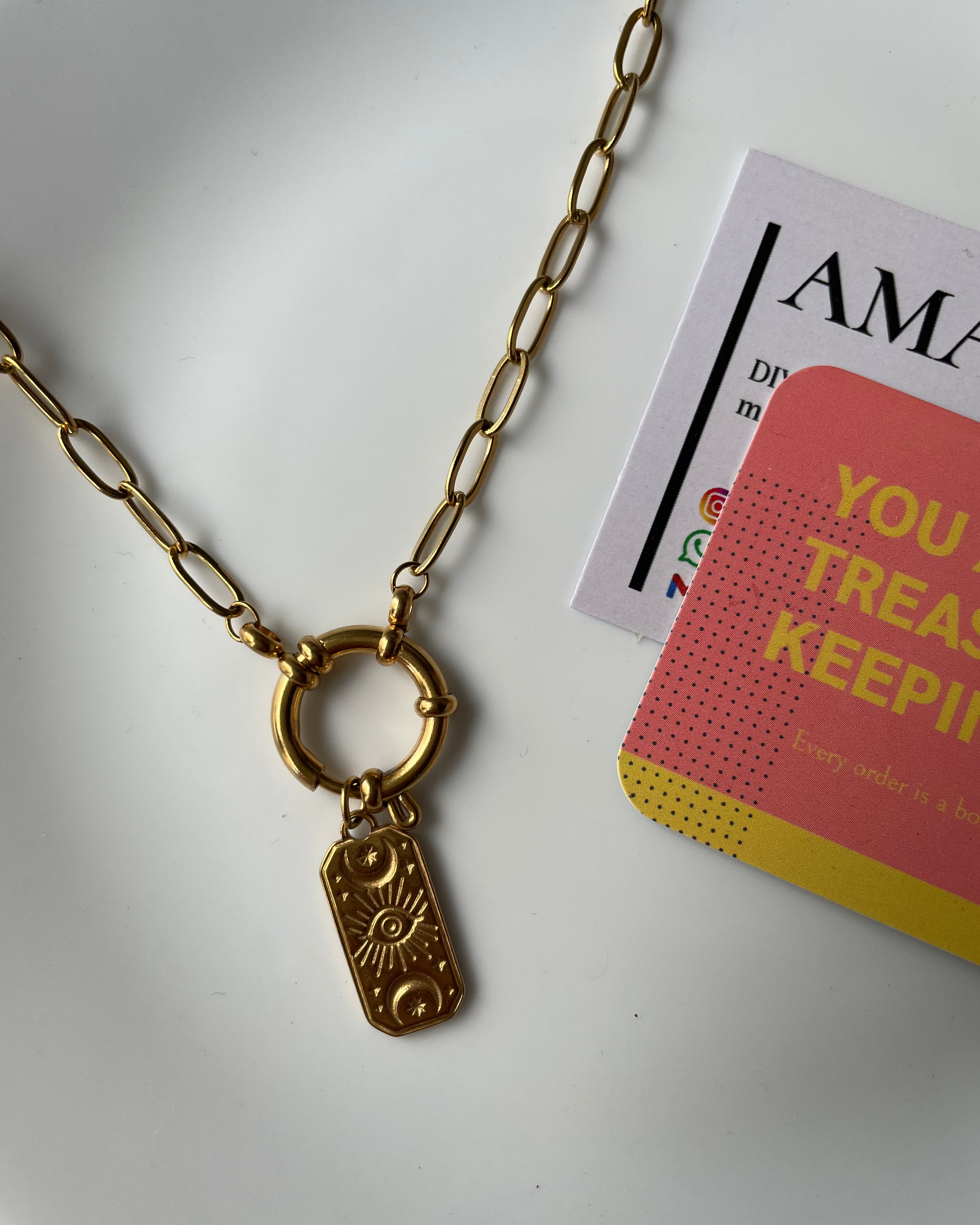 Gold necklace with a pendant on a white surface next to a book titled 'Your Treasure Keeping'.