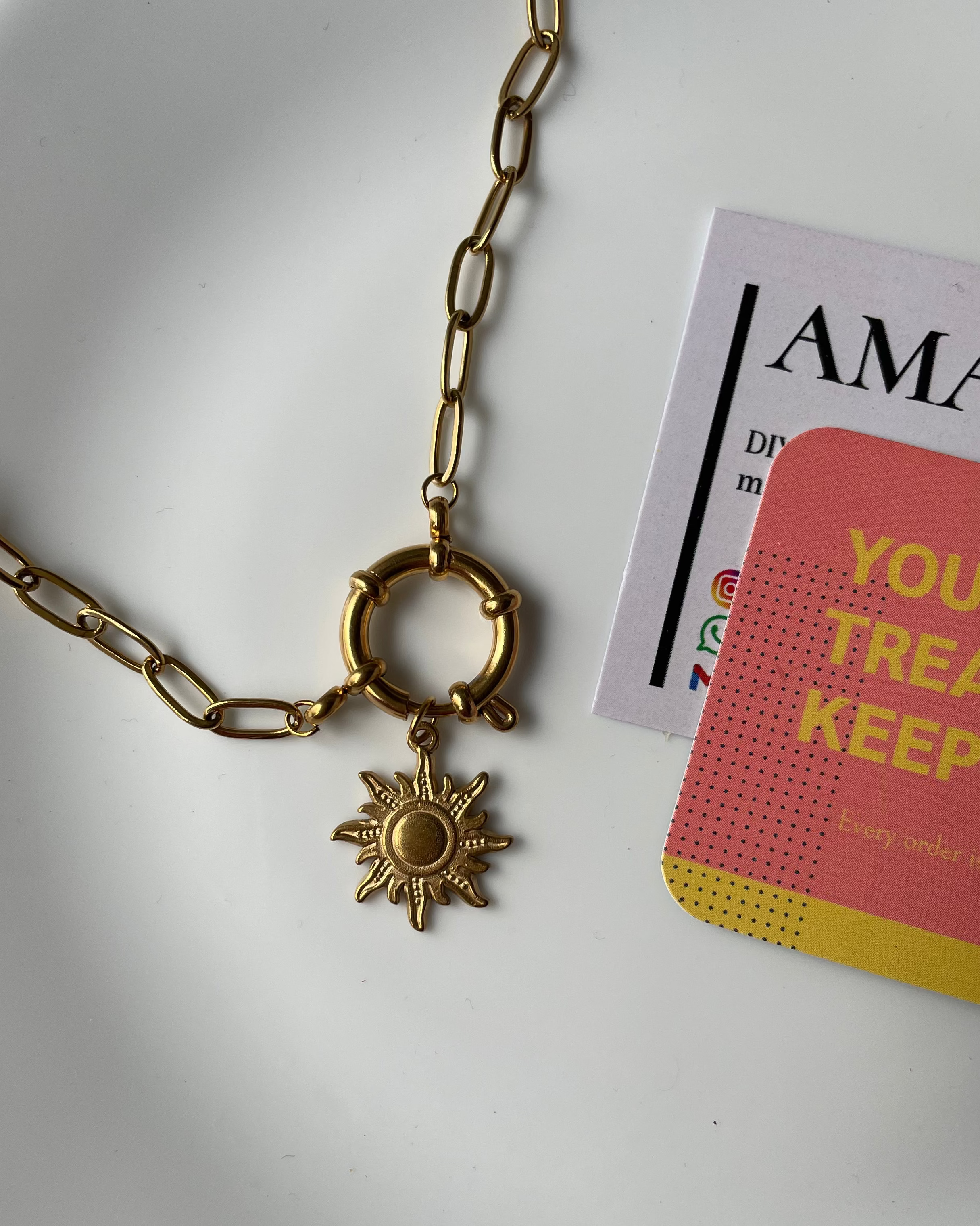 Gold necklace with a sun pendant on a white plate with a magazine underneath