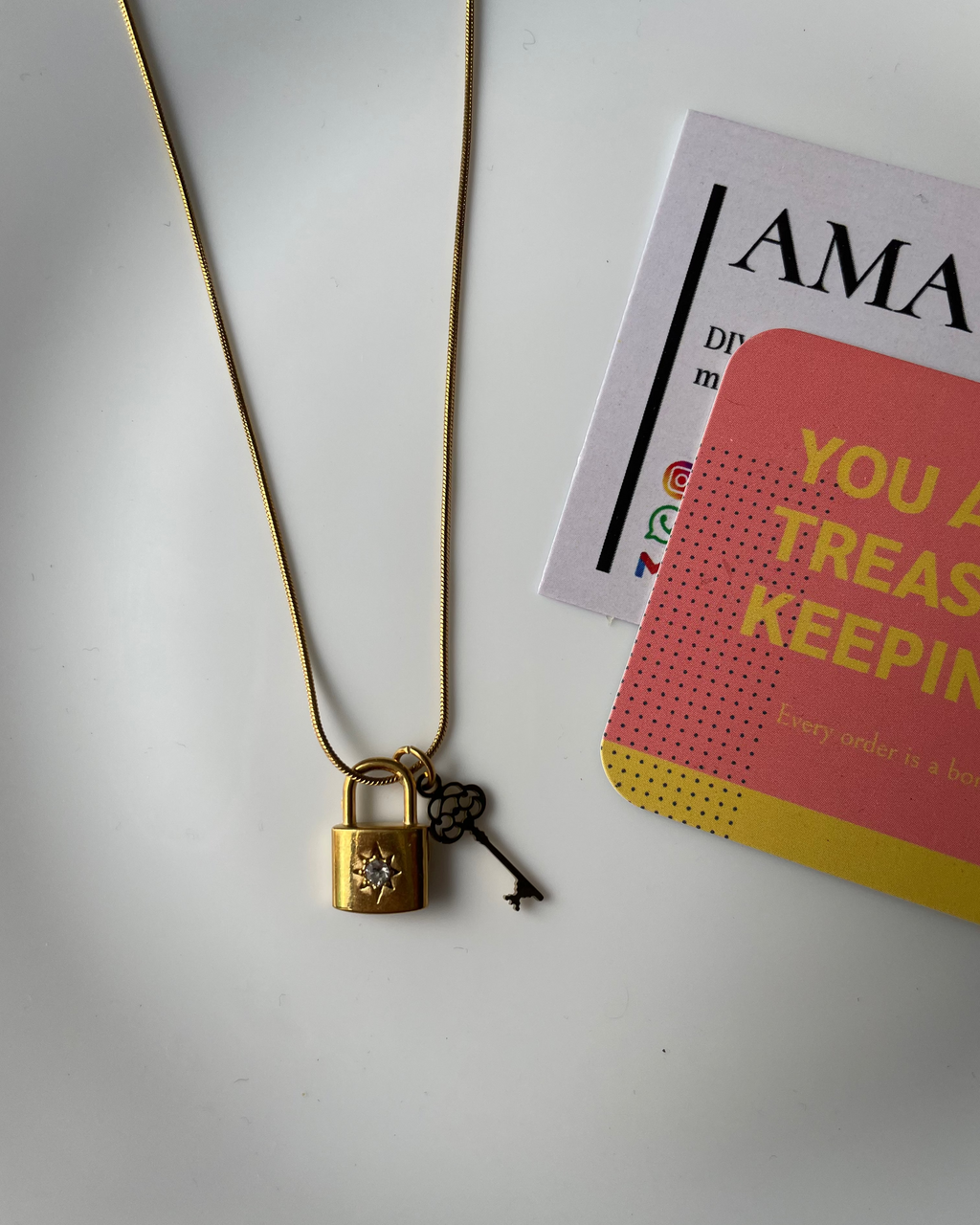 Gold necklace with a decorative clasp on a white surface with a card in the background.