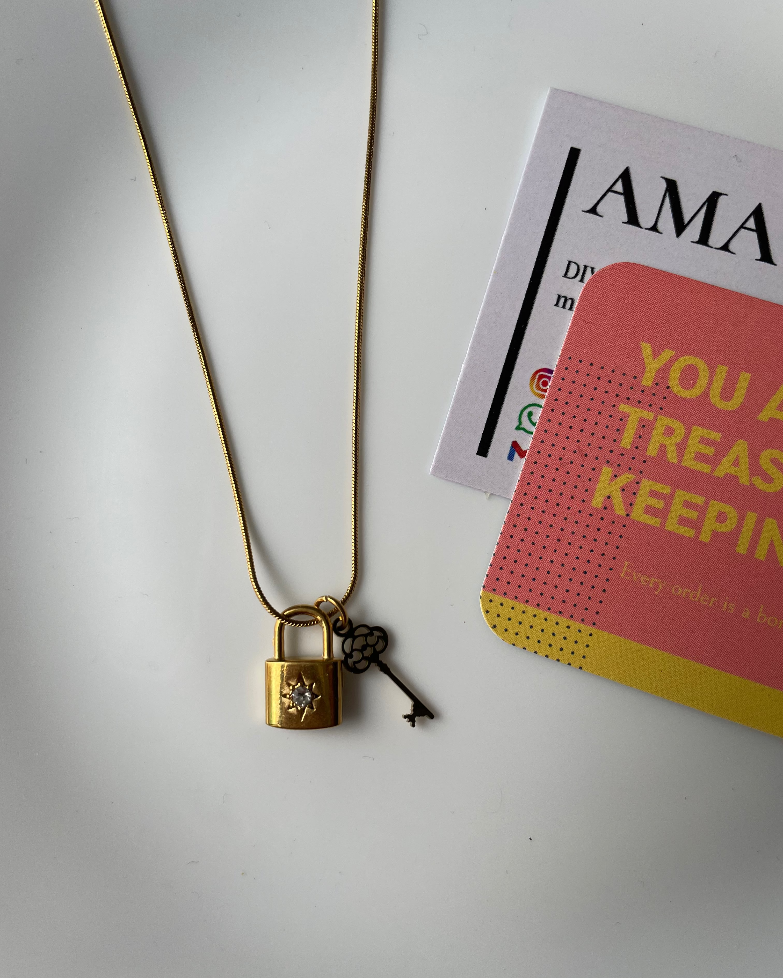 Gold necklace with a decorative clasp on a white surface with a card in the background.