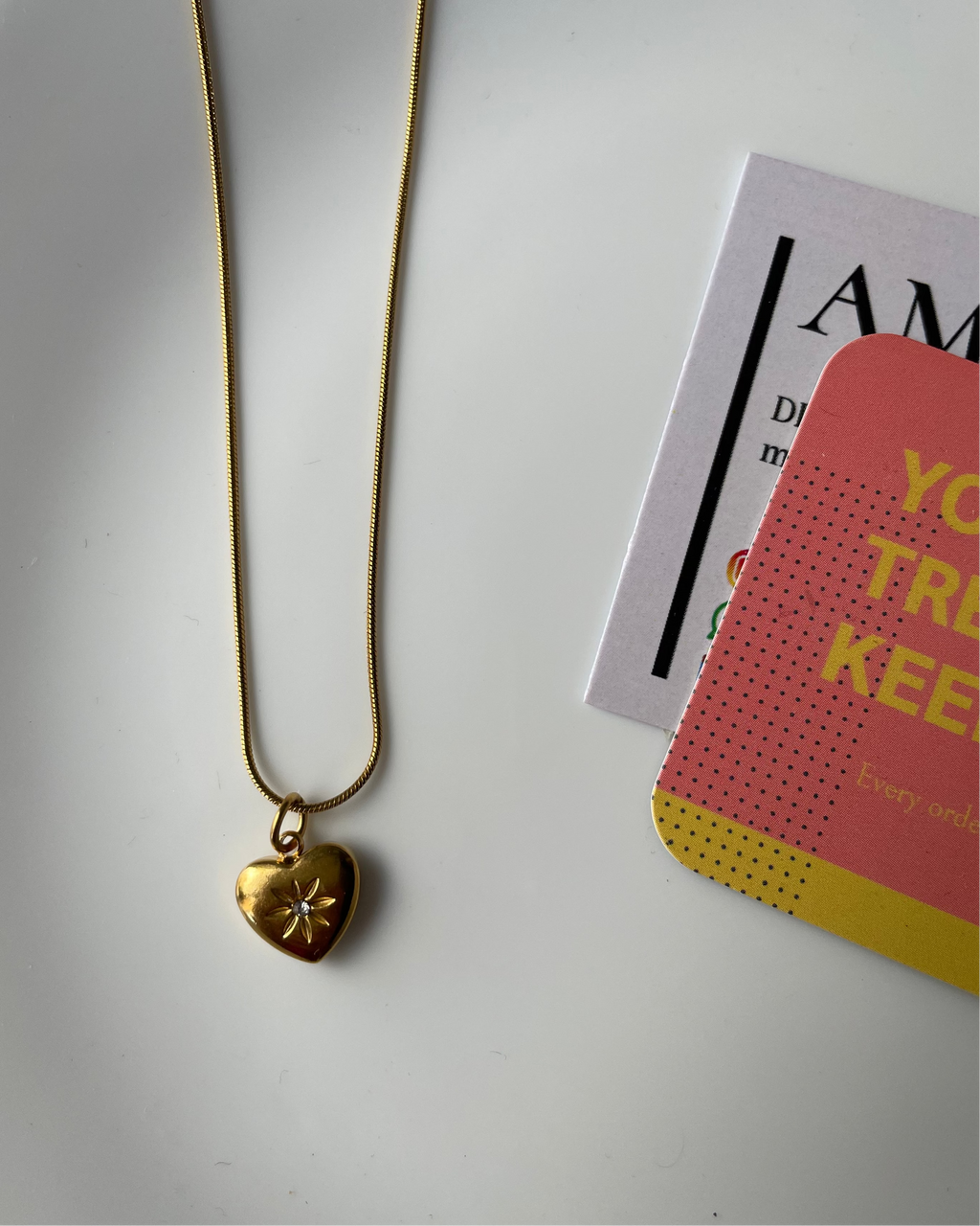 Gold necklace with a heart-shaped pendant on a white surface with a magazine.