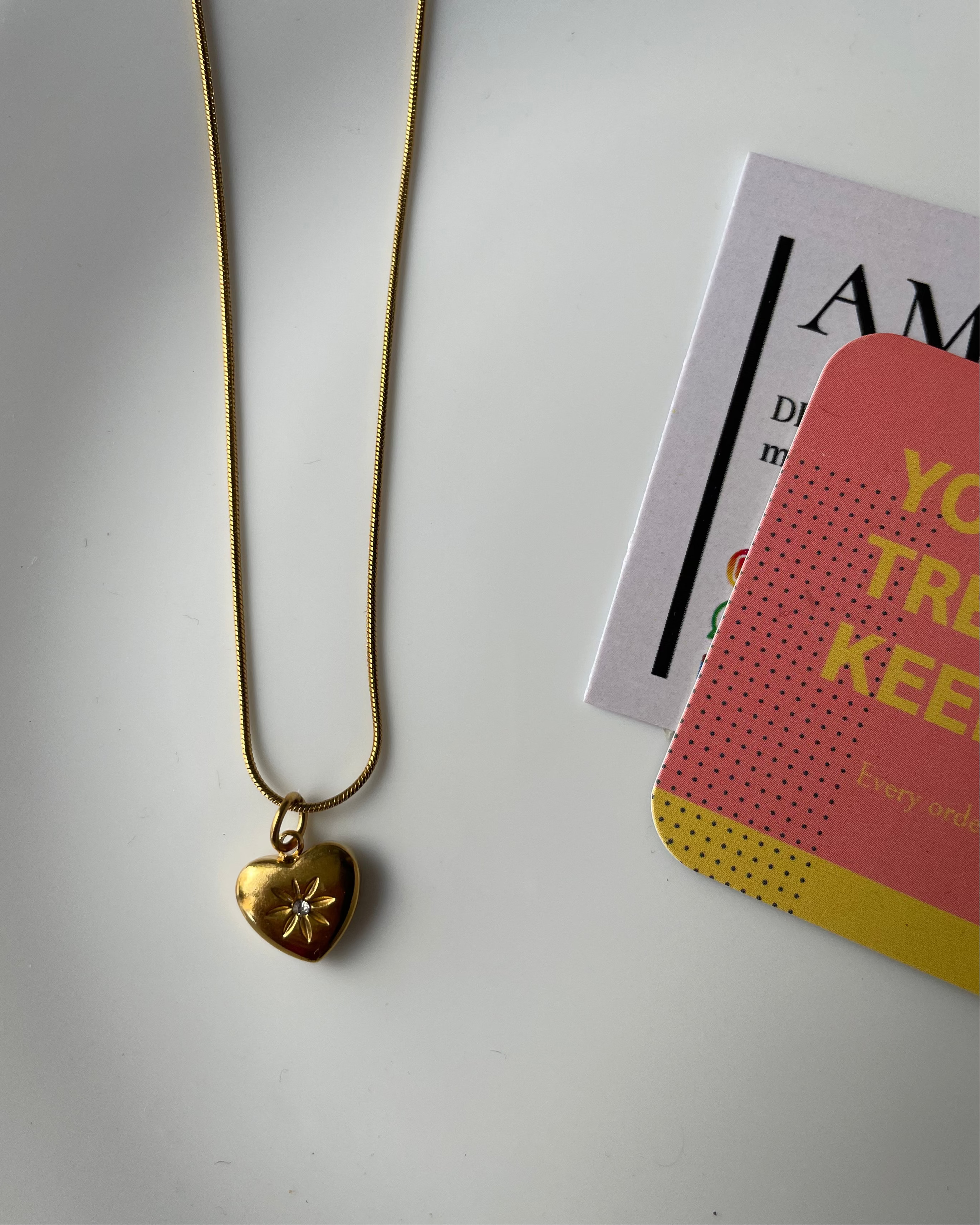 Gold necklace with a heart-shaped pendant on a white surface with a magazine.