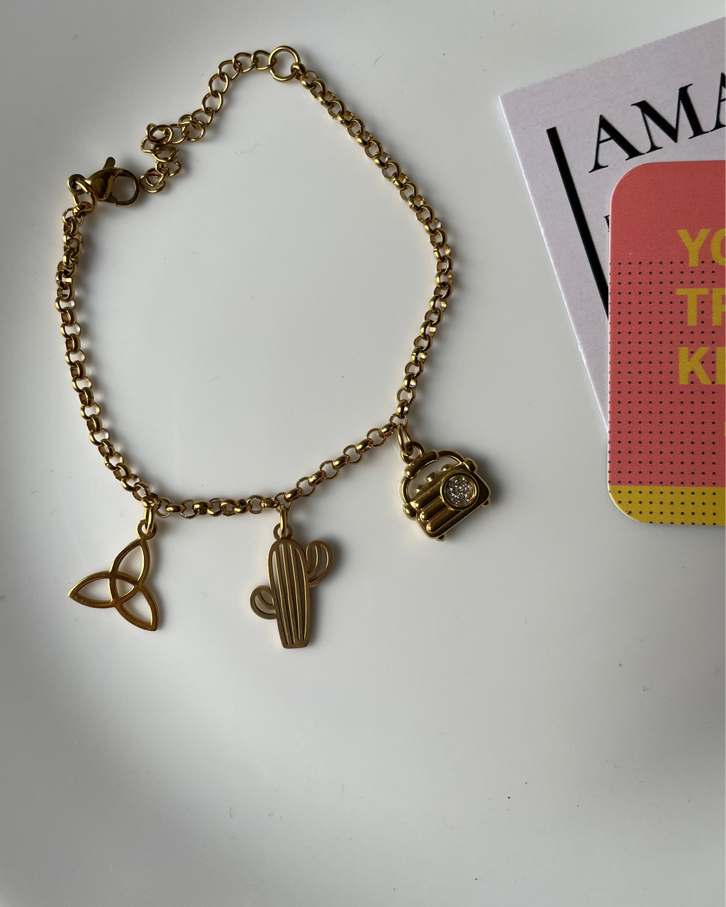Gold bracelet with charms on a white surface next to a magazine
