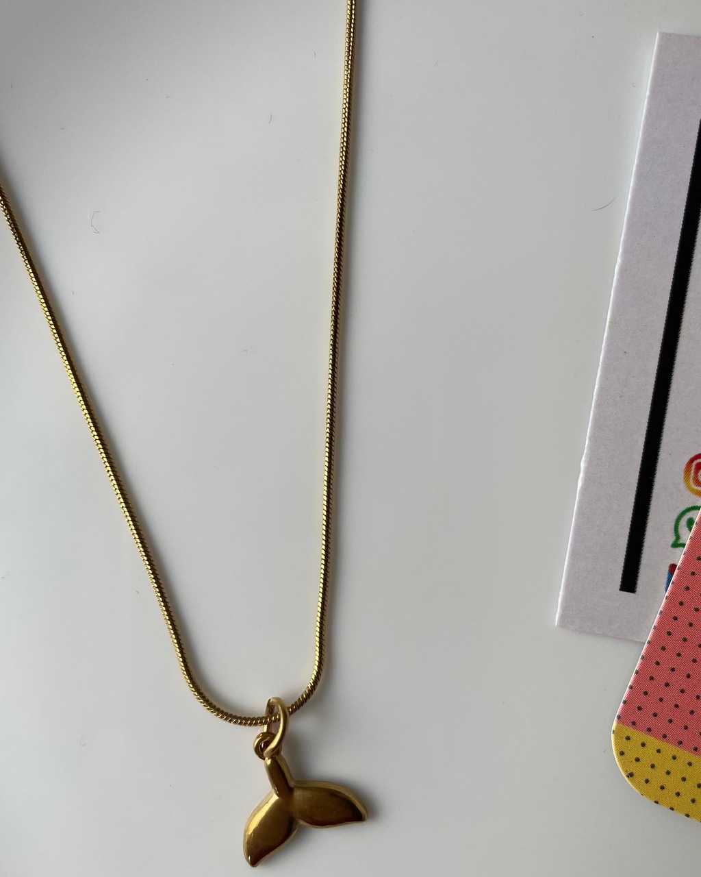 Gold necklace with a leaf pendant on a white surface with a magazine in the background.