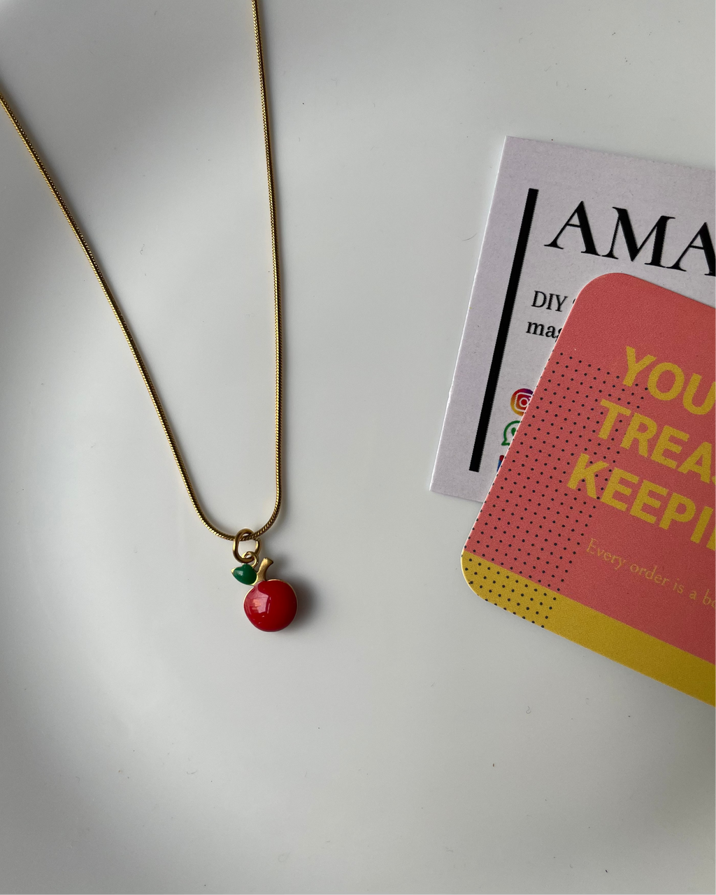 Necklace with a red pendant on a white surface next to a magazine