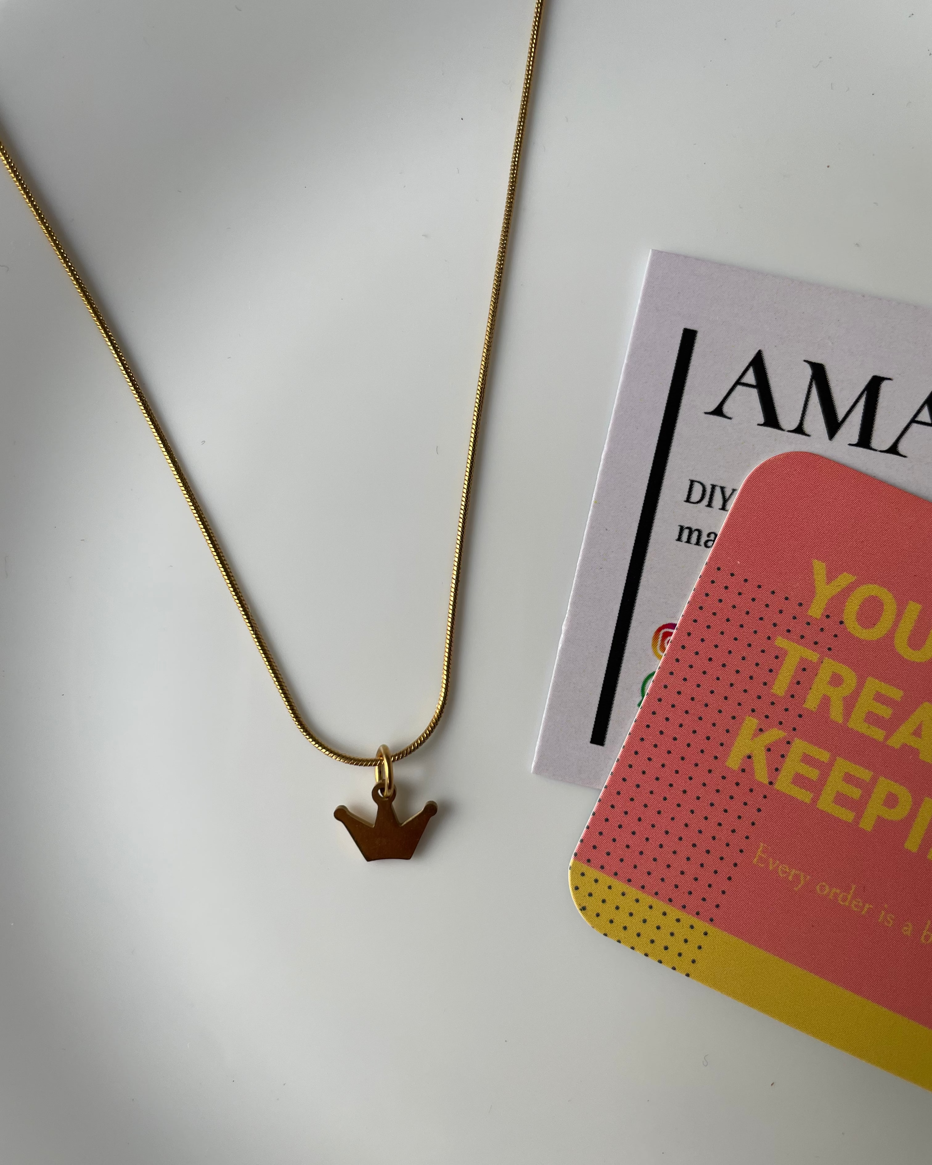 Gold necklace on a white surface with a magazine in the background