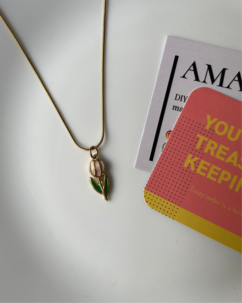 Gold necklace with a green pendant on a white surface with promotional materials in the background.