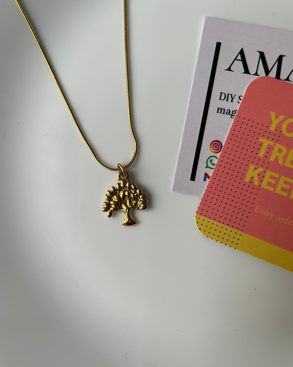 Gold necklace with a leaf-shaped pendant on a white surface with magazine in the background
